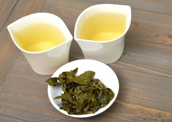 two white leaf shaped tea cups with golden infusion and wet leaves on a white tray